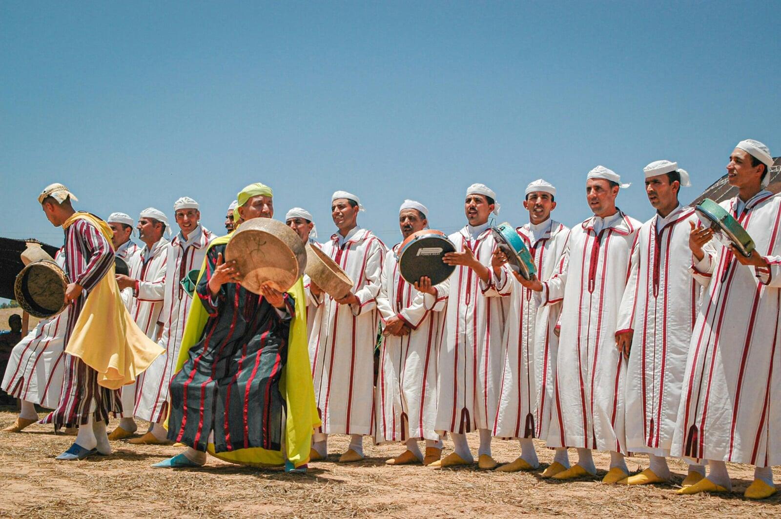 Traditional Moroccan Ahidous dance in the Atlas Mountains, with Amazigh men and women standing in a circle, clapping and singing in unison during a village celebration