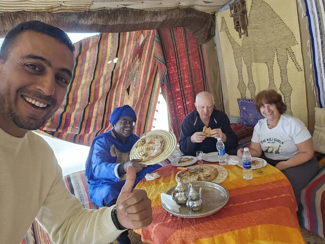 Driver-guide and two travellers sharing Berber pizza and mint tea in a desert tent