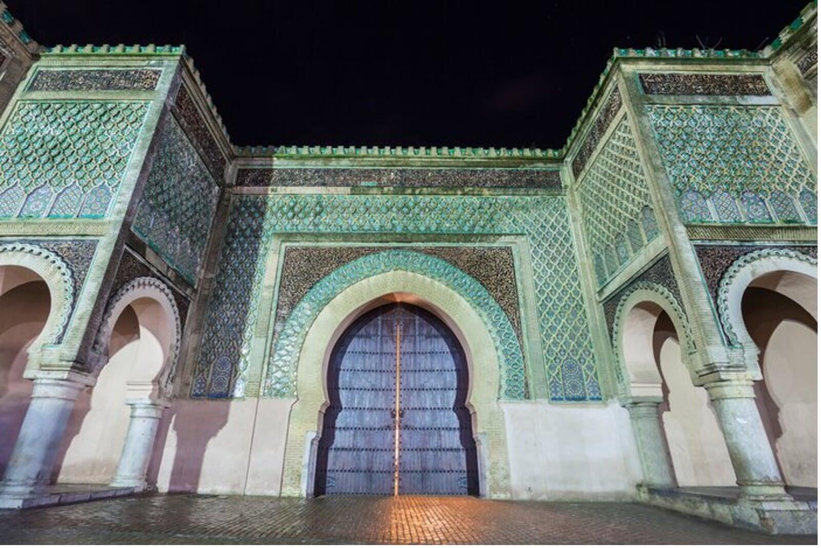 Bab Mansour gate in Meknes with its grand horseshoe arch, green-and-white zellige tiles and carved inscriptions facing lively Place el-Hedim.