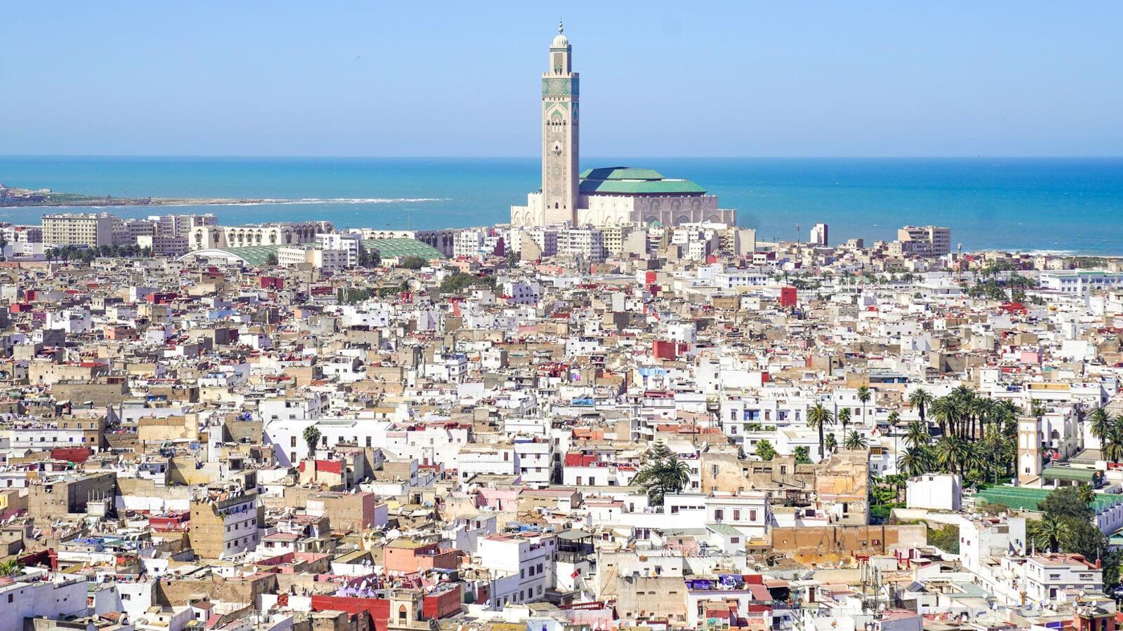 Panoramic view of Casablanca’s medina with white city rooftops leading to the oceanfront Hassan II Mosque and its tall minaret rising above the Atlantic