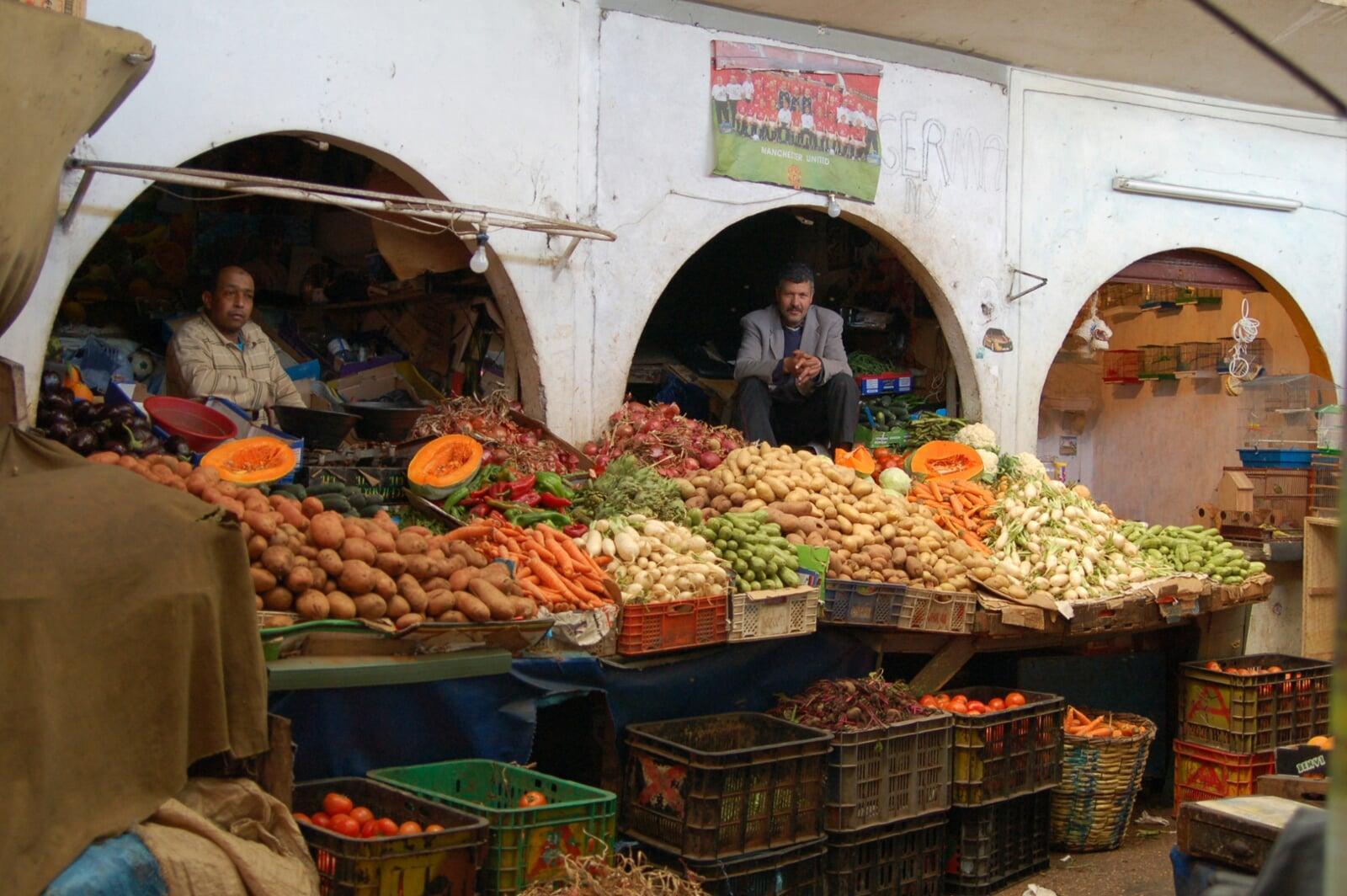 Colorful Moroccan market souk with two local men shopping for fresh vegetables during a guided Morocco tour.